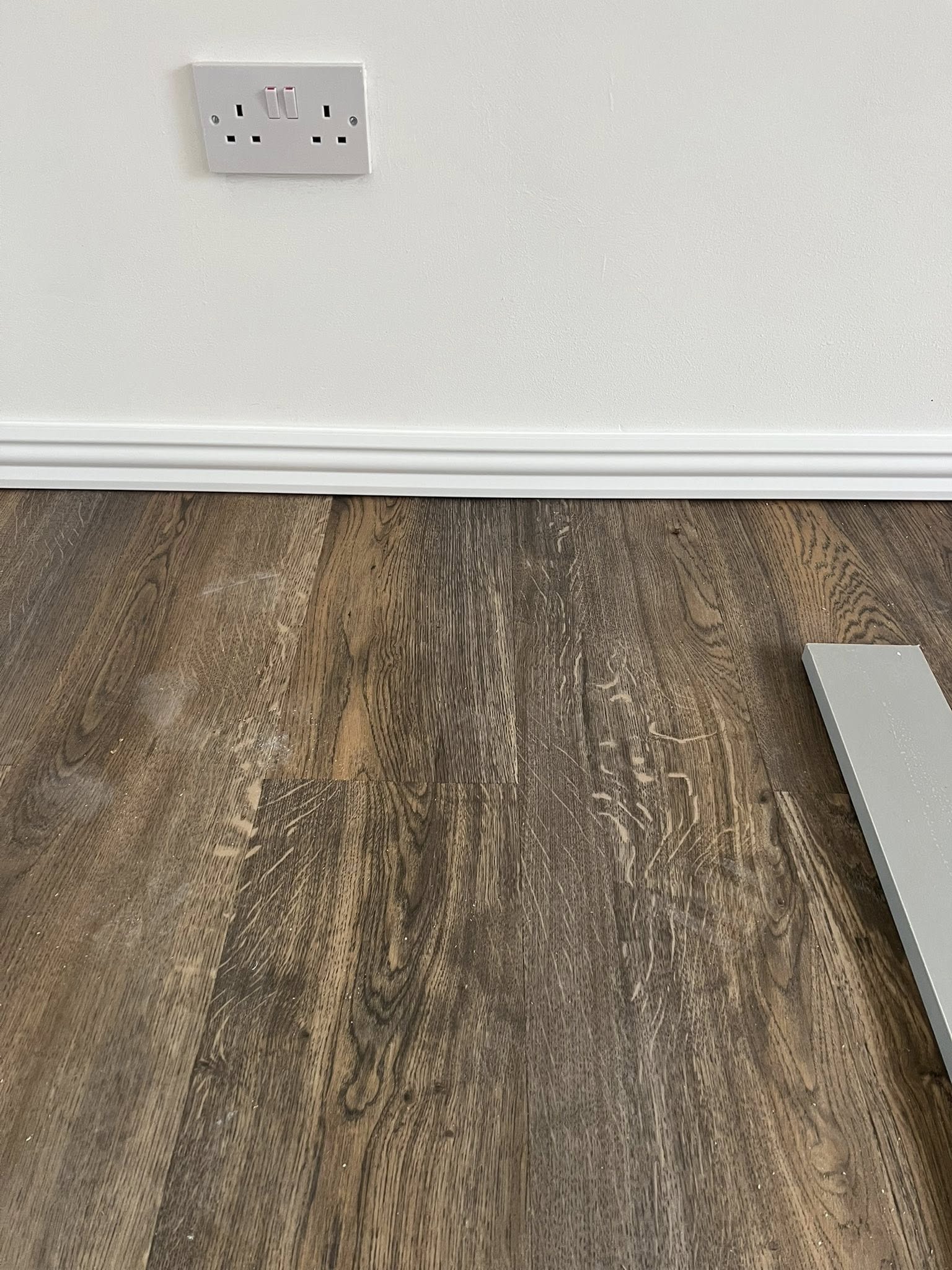 Dark wood flooring meeting white skirting and wall socket